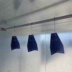 Three dark blue metal shield-like guards hanging from a horizontal metal rod against a light gray wall.