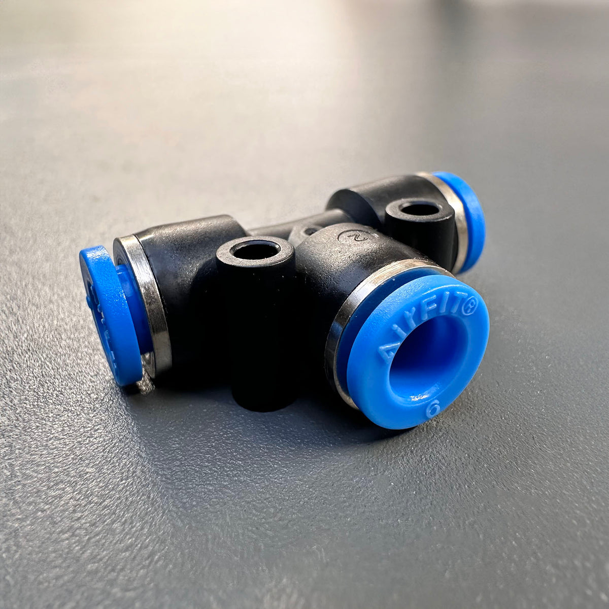 A black T-shaped pneumatic push connector with blue accents, featuring male BSP threaded fitting on one end.