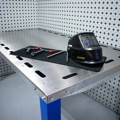 Welding helmet and tools on a Nukeson industrial downdraft table with a patterned wall in the background