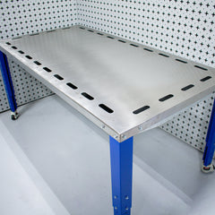 Industrial custom downdraft table workbench with blue legs against a patterned wall.