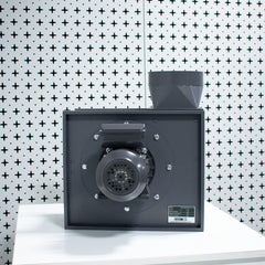Black rectangular centrifugal fan on a white surface with a patterned wall in the background