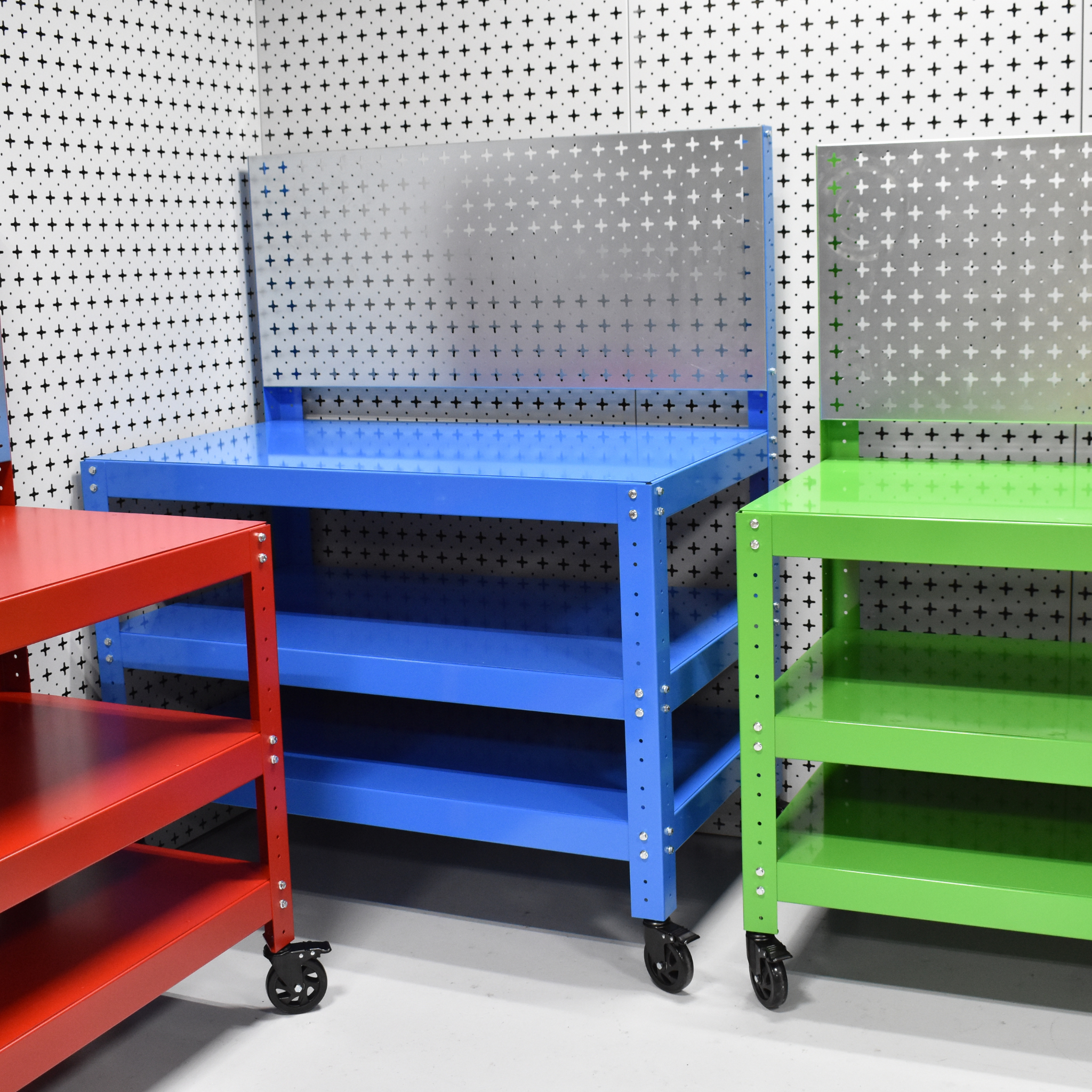 Three colorful metal workbenches (red, blue, green) against a pegboard wall.