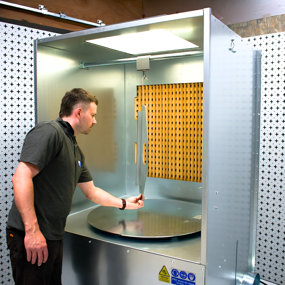 Industrial ATEX spray booth with turntable on white and black background with person hanging item