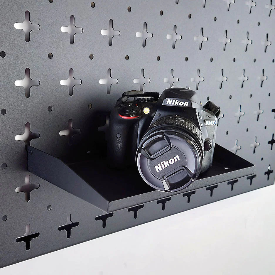 A Nukeson Tool Wall black universal shelf, with a camera, which is attached to a black wall organiser