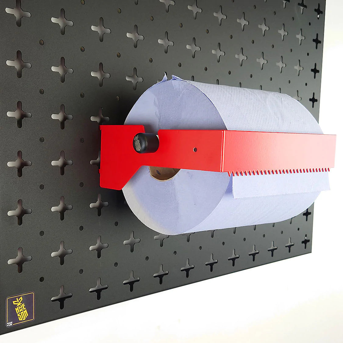 A Red, blue roll holder with a blue roll in it, mounted on a black wall, designed to be used with Nukeson Tool Wall Organiser Panels.