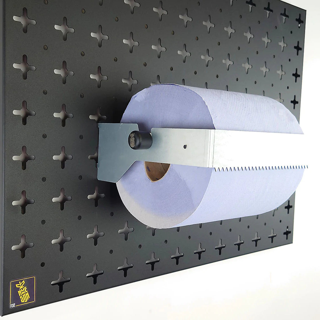 A galvanised steel, blue roll holder with a blue roll in it, mounted on a black wall, designed to be used with Nukeson Tool Wall Organiser Panels.