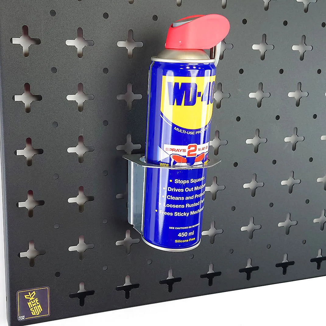 A Nukeson Tool Wall galvanised steel aerosol can holder attachment, mounted on a black wall, with a blue can with red spray nozzle inserted