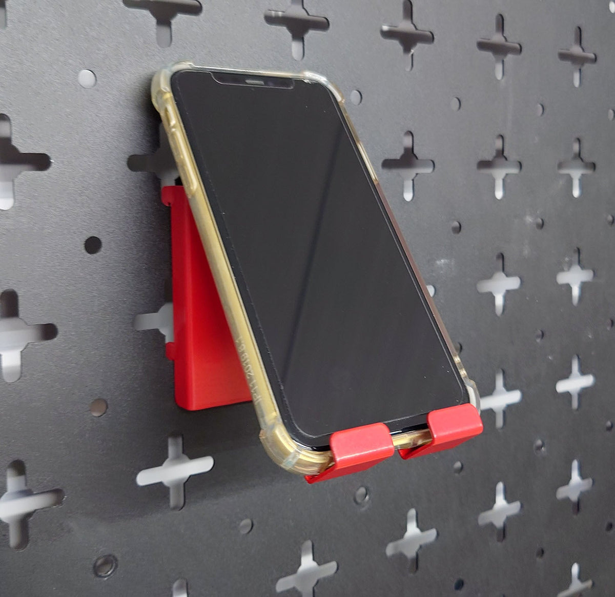 Red Nukeson Peboard Tool Wall phone holder attatchment, with phone, on a black pegboard wall